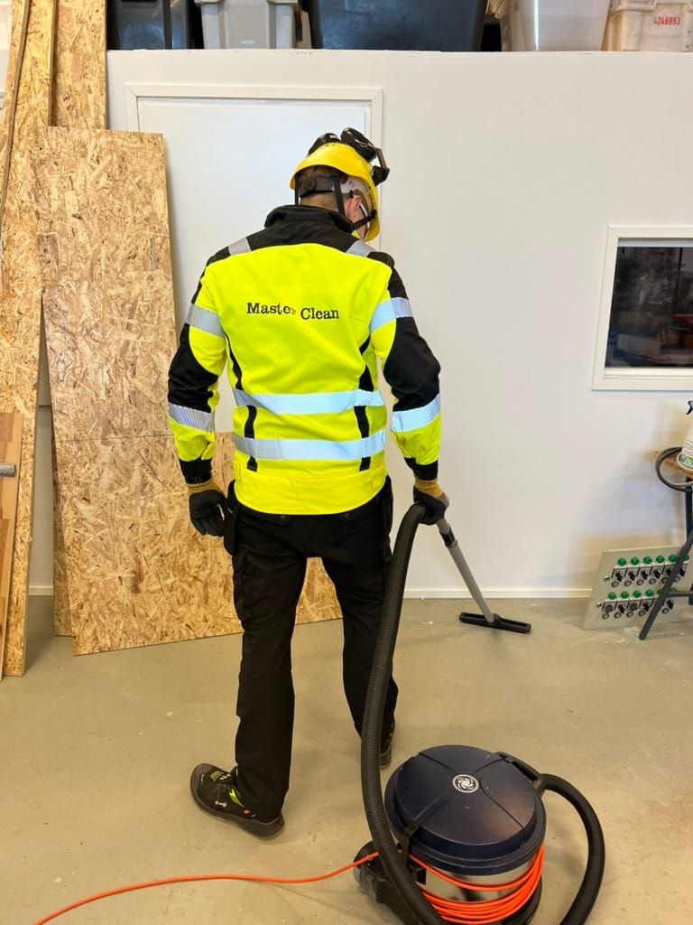 Siivooja imuroi rakennuskohdetta huomiovaatteissa